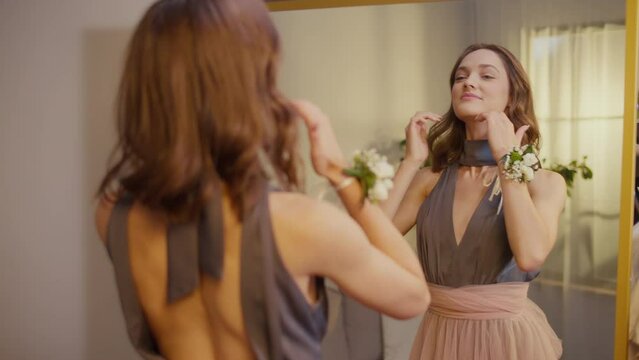 Back View of Pretty Young Woman Corrects Her Appearance in Front of the Mirror.An Attractive Girl Getting Ready for an Event, Prom. Femininity and Elegance. Festive Mood.