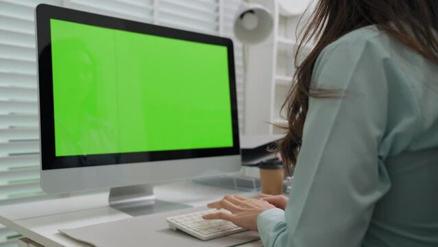 Asian businesswoman typing using keyboard on desktop computer green screen monitor in the office room. Projects manager work hard with pile of document on table in office. Work and career concept