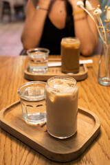 An iced latte on a table in a cafe. A girl with a phone in her hands is sitting in the background.