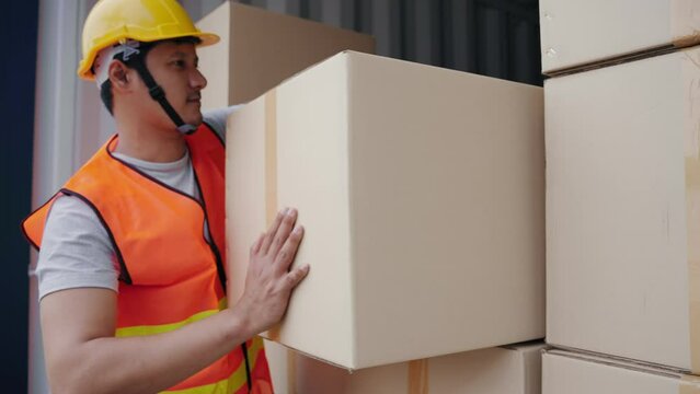 Strong Asian worker lifting and stacking many boxes of goods in containers at the transportation warehouse. Cargo container and Transport Logistic concept