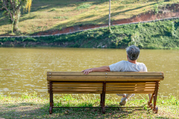 Naklejka na ściany i meble Loneliness Asian senior man sitting alone on outdoor bench in public park. Depressed elderly retirement male feeling lonely, sad and boredom. Old people mental health, illness recovery concept