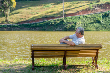 Loneliness Asian senior man sitting alone on outdoor bench in public park. Depressed elderly retirement male feeling lonely, sad and boredom. Old people mental health, illness recovery concept
