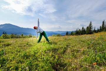 Wman doing yoga on blossom meadow and mountains background. Morning healthy activity.