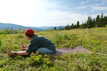 Naklejka na ściany i meble Wman doing yoga on blossom meadow and mountains background. Morning healthy activity.