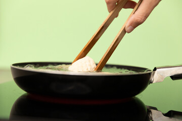 Putting a croquette with woodens tweezers into a frying pan on green background