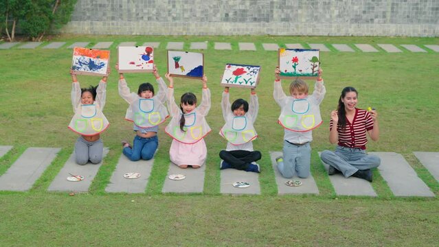 Group of diverse elementary students and female teacher learn art and drawing poster color outdoors at lawn. Children use time to activity creativity during school lesson in park at elementary school.