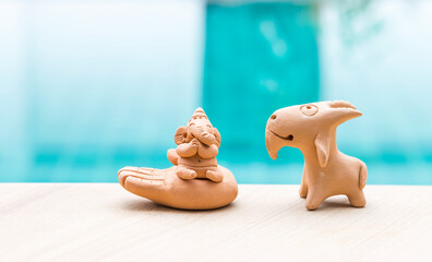 Elephant clay sculpture with goat clay sculpture over blurred blue water background, outdoor day...