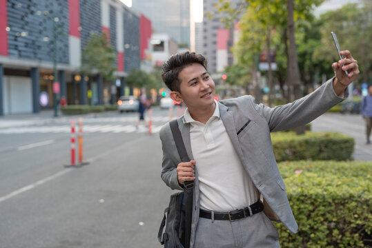 A young male office worker takes a selfie with his cellphone while taking a walk to work in the city.