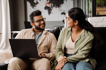 Fototapeta premium Indian colleagues using laptop while sitting on couch in office