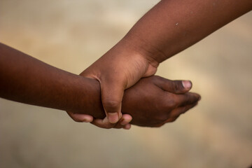 A boy holds the fingers of another boy with his hands and the background is blurred behind them