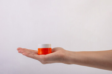 Plastic orange tube for cream or lotion. Skin care or sunscreen cosmetic in hand on white background.