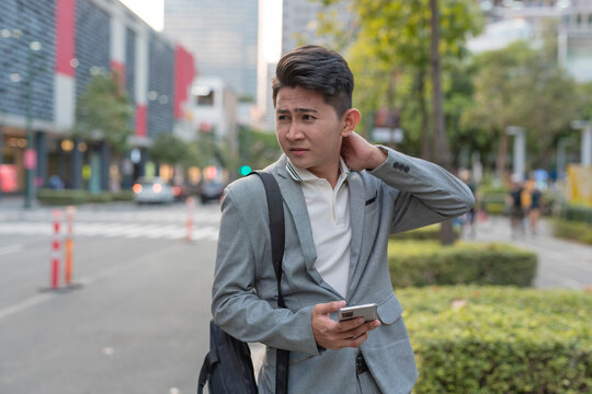 A young asian man suffers from a stiff neck while walking to work. Urban city setting.