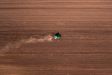 Agricultural tractor with tiller attached performing field tillage before the sowing season, aerial...