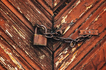 Old rusty corroded padlock with chain on wooden farm barn door - Powered by Adobe
