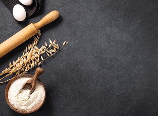 Oatmeal, eggs and rolling pin on a dark  background. Organic baking ingredients. Concept of...
