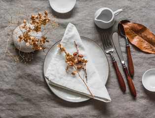The idea of an autumn dining table setting with ceramic dishes, dried flowers, linen tablecloth and napkins, top view