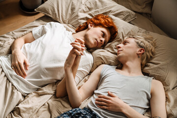 Gay couple holding hands and looking at each other while laying on bed