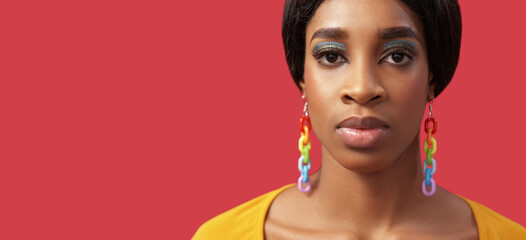 Lgbt portrait. Diversity colors. Equality right. Confident proud woman face bright makeup rainbow earrings on pink empty space background.