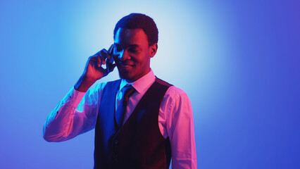 Business call. Neon people. Mobile communication. Confident smiling man speaking on phone in pink color light on blue gradient empty space background.