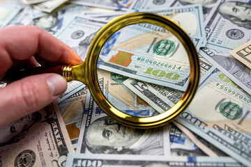 Male hand hold magnifying glass over US dollar bill