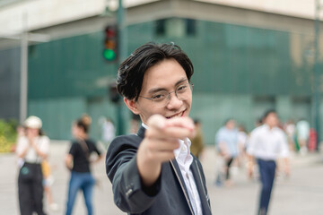 A young confident corporate asian man in his early 20s points a finger to the camera. Outdoor city...