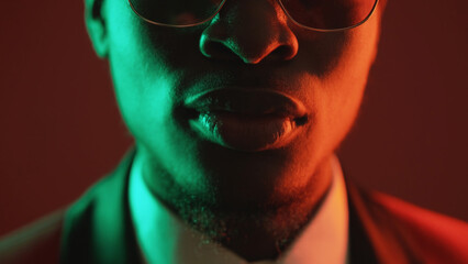 Neon face. Masculine determination. Green red color light closeup portrait of serious confident man in tuxedo suit glasses on dark.