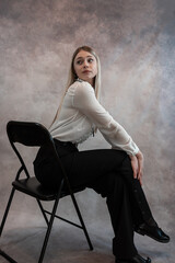 Pretty woman wear white blouse and black pants sitting on chair and looking at camera, studio shoot