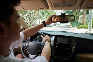Driver adjusting rearview mirror when driving to work in city street