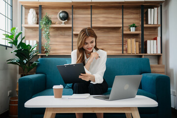 Fototapeta na wymiar Young attractive Asian woman smiling thinking planning writing in notebook, tablet and laptop working from home at office .