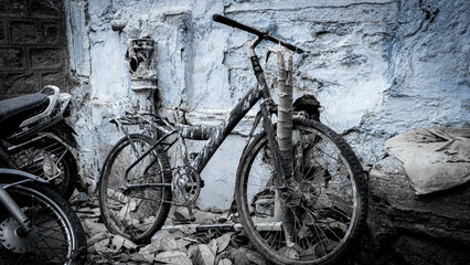 Old bicycle leaning against a blue stone wall dirty and full of paint reflecting abandonment, loneliness and sadness