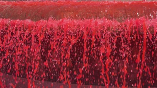 Red flowing liquid colored fountain water with bright waterfall jets in slow motion