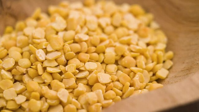 Dried crushed yellow fava beans falling into a wooden rustic bowl in slow motion. Shredded uncooked legumes close up. Rotation