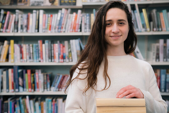 Young librarian standing with books in library