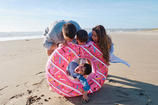 Playful family with pink doughnut shaped inflatable ring at beach