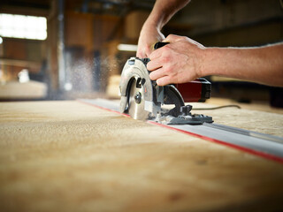 Carpenter cutting wooden board with circular saw in workshop