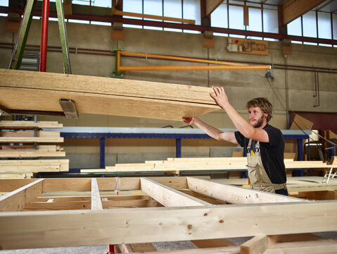 Carpenter holding oriented strand boards on crane in workshop