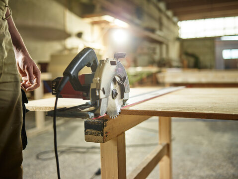 Carpenter with circular saw on oriented strand board in workshop