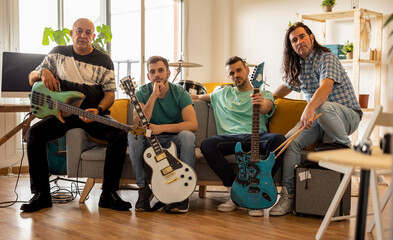 Rock musicians sitting with guitars and drumsticks on sofa at home