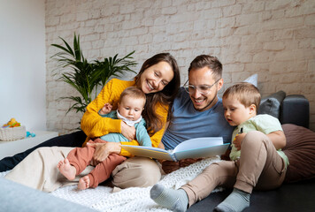 Happy parents reading book for children on couch at home