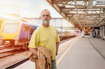 Fototapeta premium Traveler with a suitcase and suit waiting for a train at the train station. Travel concept.