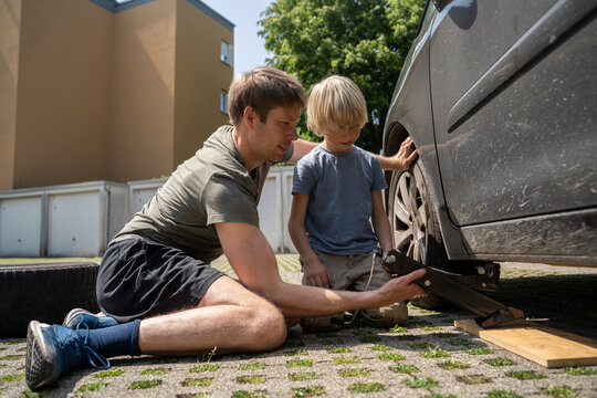 Boy watching father changing car tire in yard