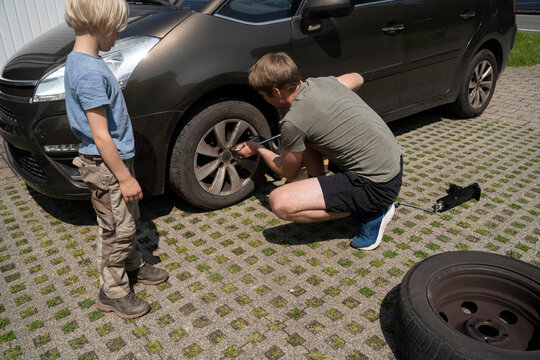 Boy watching father repairing car tire in yard
