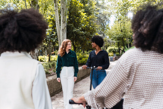 Happy young woman riding electric push scooter and spending time with friends