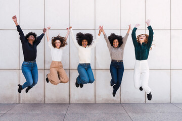 Happy businesswomen together jumping in front of wall
