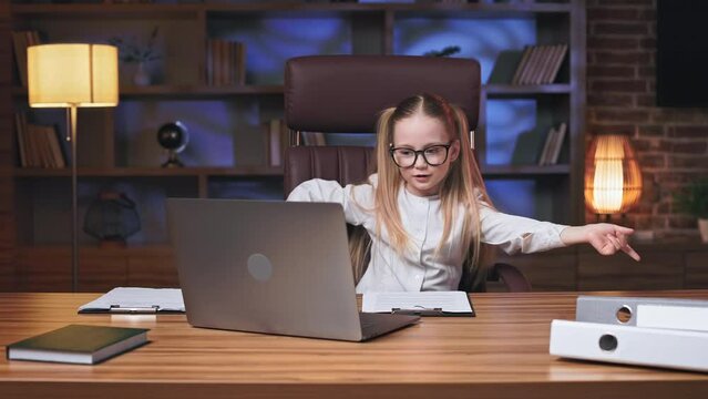 Vibrant blonde kid chilling out and listening to drive music on wireless laptop in coworking space. Energetic little girl moving rhythmically hands while resting on comfortable office chair.