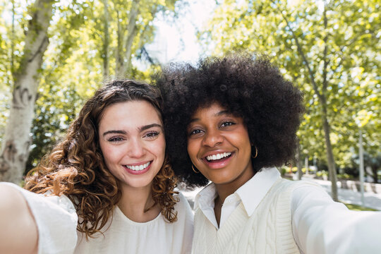 Happy multiracial friends taking selfie together in park