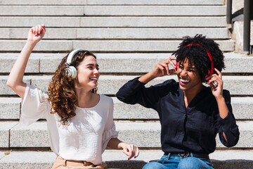 Cheerful woman listening to music and enjoying with friend on sunny day