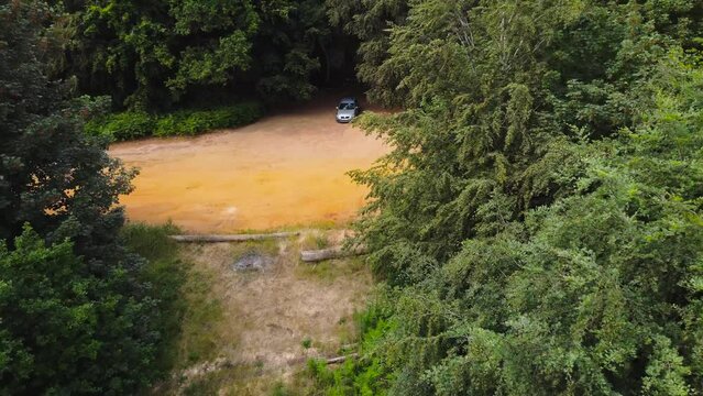 A cinematic aerial push-back shot of a car inside a forest full of green trees near Norfolk England morning 