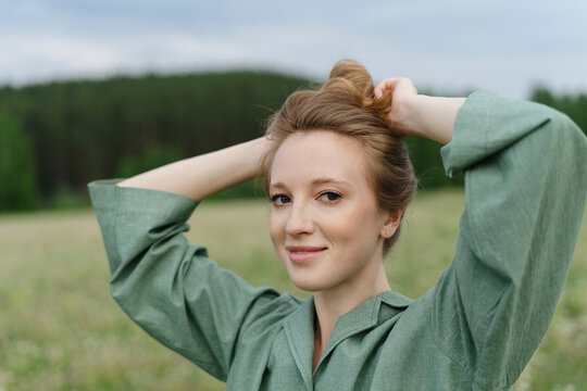 Smiling young woman tying hair bun on field
