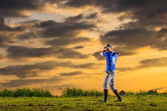 Young baseball player taking shot standing on grass at dusk